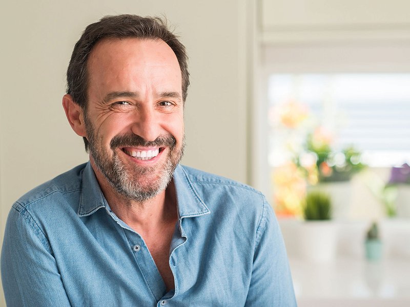 Hombre sonriendo con ventana y flores detrás