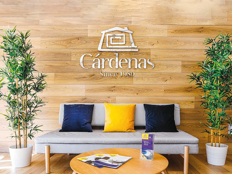 Sofá con cojines azules y amarillo y logo de Cárdenas sobre pared de madera