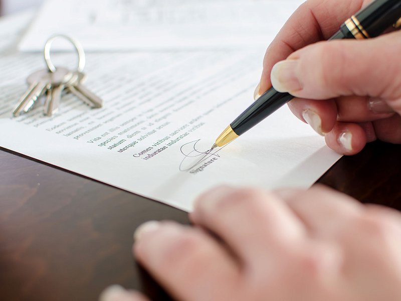 Signing a contract in the foreground with keys on top of it