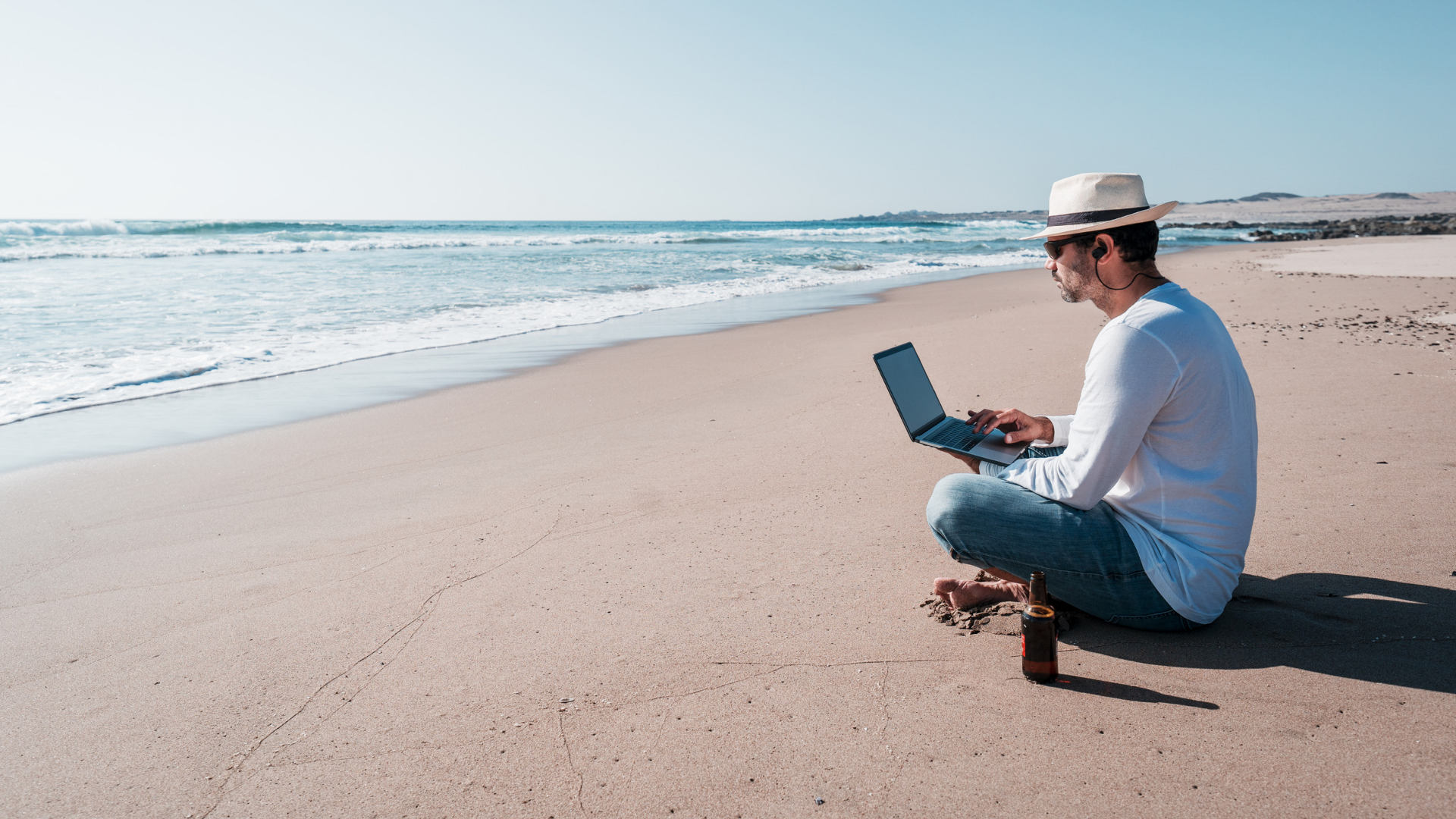 Mann arbeitet mit Laptop am Strand