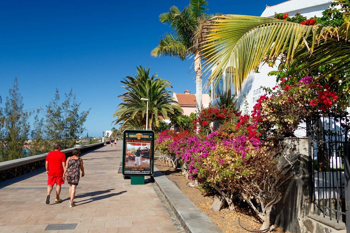 Playa del Inglés, Gran Canaria, Paar auf der Promenade neben Häusern mit Bunganvillas
