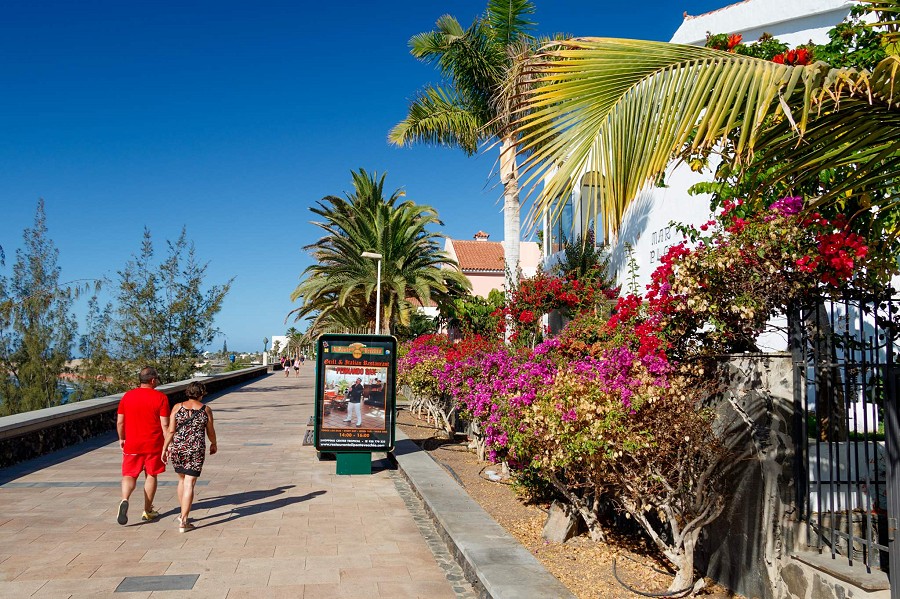 Playa del Inglés, Gran Canaria, couple marchant le long de la promenade à côté de maisons avec bunganvillas